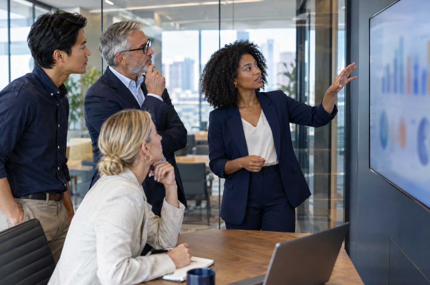 Four colleagues around a screen in a glass meeting room, mid-discussion